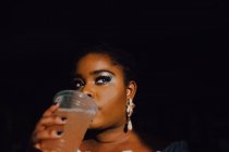 Belle jeune femme noire incurvée avec un maquillage lumineux en robe hors épaule ayant une boisson froide — Photo de stock