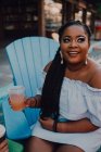 Afro-américaine jeune femme boire une boisson froide tout en étant assis au café hipster, détournant les yeux — Photo de stock