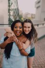Jeunes femmes décontractées multiraciales riant et se câlinant debout dans la rue regardant la caméra — Photo de stock