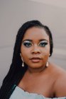 Attraktive schwarze junge Frau mit hellem Make-up im Off-Shoulder-Kleid steht auf einer leeren Wand und blickt in die Kamera — Stockfoto