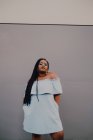 Jolie jeune femme noire avec un maquillage lumineux en robe hors épaule debout sur un mur vide, regardant la caméra — Photo de stock