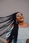 Sorridente giovane donna nera con brillante make-up in off-spalla abito flipping trecce mentre in piedi sulla strada — Foto stock