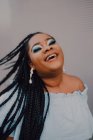 Sorridente giovane donna nera con brillante make-up in off-spalla abito flipping trecce mentre in piedi sulla strada — Foto stock