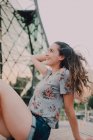 Calma contenuto casual giovane donna in pantaloncini e t-shirt godendo di sole mentre seduto sul parapetto di cemento, guardando altrove — Foto stock