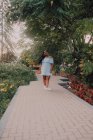Noir jeune femme avec de longues tresses en robe hors épaule sur le chemin de béton dans le jardin en fleurs regardant caméra — Photo de stock