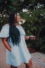 Attraente giovane donna nera con trucco luminoso in abito da spalla ascoltando musica su smartphone con auricolari — Foto stock