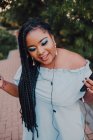 Attraktive schwarze junge Frau mit hellem Make-up im Off-Shoulder-Kleid, die mit Kopfhörern Musik auf dem Smartphone hört — Stockfoto