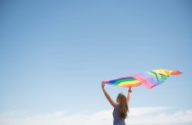 Side view of adult confident woman in casual dress carrying rainbow colored flag above head on windy day — Stock Photo