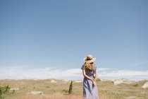 Задний вид взрослой женщины в платье с огоньком сухих травяных шипов, стоя на живописном поле, Нида — стоковое фото