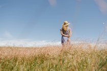 Rückansicht einer erwachsenen Frau im Kleid mit einem Hauch trockener Grasdornen im Stehen auf einem landschaftlich reizvollen Feld, nida — Stockfoto