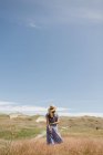 Schnittrückseite Ansicht einer erwachsenen Frau im Kleid mit einem Hauch trockener Grasdornen, während sie auf einem landschaftlich reizvollen Feld steht, nida — Stockfoto