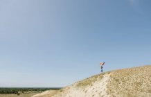 Vue latérale de la femme confiante adulte en robe décontractée portant drapeau de couleur arc-en-ciel au-dessus de la tête le jour du vent — Photo de stock