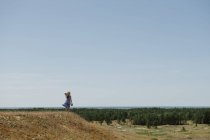 Back view of adult woman in straw hat and dress with camera standing on hill — Stock Photo