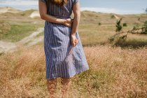 Image recadrée de la femme adulte en robe avec une torsion de pointes d'herbe sèche tout en se tenant debout sur le champ pittoresque, Nida — Photo de stock