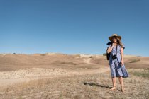 Adult woman in straw hat and dress with camera standing on country path — Stock Photo