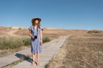 Donna adulta in cappello di paglia e vestito con macchina fotografica in piedi sul sentiero di campagna — Foto stock