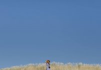 Back view of adult woman in straw hat and dress with camera standing on hill — Stock Photo