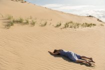 Женщина в повседневной одежде лежит лицом вниз на песчаной дюне в жаркий летний день — стоковое фото