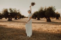 Zufriedene Frau im Kleid mit offenem Rücken, erhobene Hände mit Blumenstrauß — Stockfoto