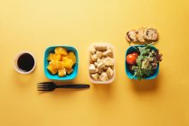 Draufsicht auf Lebensmittelbehälter mit Brot und Tomaten, Rucola und Orangenstücken, Sojasauce und Hühnerfilet mit schwarzer Plastikgabel auf gelbem Hintergrund — Stockfoto