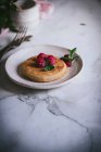 Tasty pancake topped with fresh raspberries and mint leaves on white plate on marble tabletop — Stock Photo