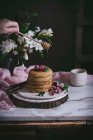 Человеческая рука капает мед на стопку блинов со свежими ягодами на фарфоре на темном фоне — стоковое фото