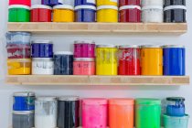 Shelves with colorful tins of paint of different shape size and colour at workplace — Stock Photo