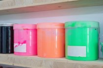 Mensole con contenitori colorati di vernice di diverse dimensioni e colori sul posto di lavoro — Foto stock
