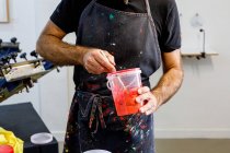 Konzentrierte Erntehelfer tragen schmutzige Schürze und mischen verschiedene Farben für Siebdruck in der Werkstatt — Stockfoto