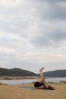 Woman doing yoga outdoors on cloudy day on dam beach — Stock Photo