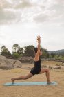 Mulher adulta média em pose alta lunge fazendo ioga ao ar livre na praia da barragem — Fotografia de Stock