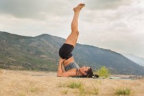 Mid adult woman in shoulderstand while doing yoga outdoors on dam beach — Stock Photo