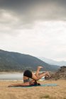 Mujer adulta con los pies arriba haciendo yoga al aire libre en la playa de la presa - foto de stock