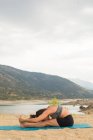 Media mujer adulta doblando mientras hace yoga al aire libre en la playa de la presa - foto de stock