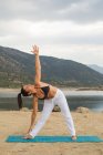 Mulher adulta média em pose triangular fazendo ioga ao ar livre na praia da barragem — Fotografia de Stock