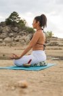 Середня доросла жінка, що медитує в лотосі йога позує на відкритому повітрі на пляжі греблі — стокове фото