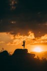 Silhouette of woman doing yoga tree pose outdoors at sunset — Stock Photo