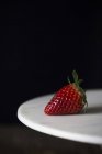Sweet ripe strawberry on white plate against black background — Stock Photo
