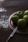 Placa de manzanas frescas verdes húmedas sobre una mesa de madera en mal estado con cuchillo - foto de stock