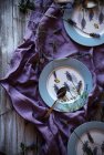 De lavandarias frescas acima colocadas em torno de placas vazias sobre tecido violeta na mesa de madeira serrada — Fotografia de Stock