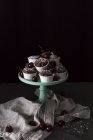 Cupcake al cioccolato e ciliegie fresche su supporto torta su sfondo nero — Foto stock