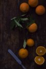 Metal knife on dark wooden tabletop near cut and whole fresh juicy oranges — Stock Photo