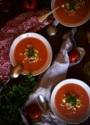 De arriba cuencos de sopa de tomate deliciosa con perejil colocado cerca de servilletas en la mesa - foto de stock