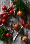 Сверху свежие спелые помидоры и лук с чесноком и петрушкой на потрепанной деревянной столешнице возле салфетки — стоковое фото