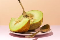 Cut ripe sweet melon on plate with spoon and fork on pink table — Stock Photo