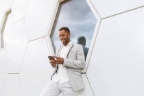 Елегантний чорний чоловік переглядає смартфон, що спирається на геометричну стіну — стокове фото