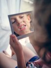 Reflexão em espelho quadrado de face de criança com bandagem na bochecha estudando dente de leite com boca aberta no quarto — Fotografia de Stock