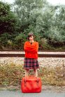 Жінка в червоному з марочний чемодан стоїть на вокзалі в сільській місцевості — стокове фото