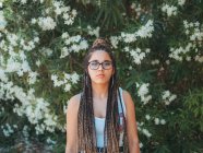 Junge Frau in Brille und Sommerkleidung steht neben blühenden Bäumen und blickt in die Kamera — Stockfoto