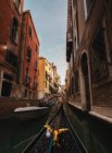Ornamental beak of gondola floating down narrow channel with old stone houses on sides — Stock Photo